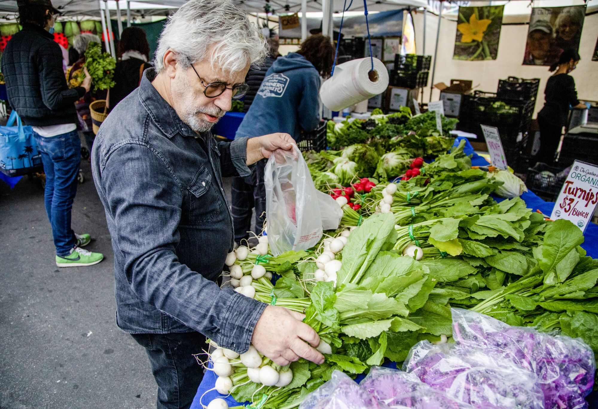 A man in round glasses picks vegetables at a farmers market.