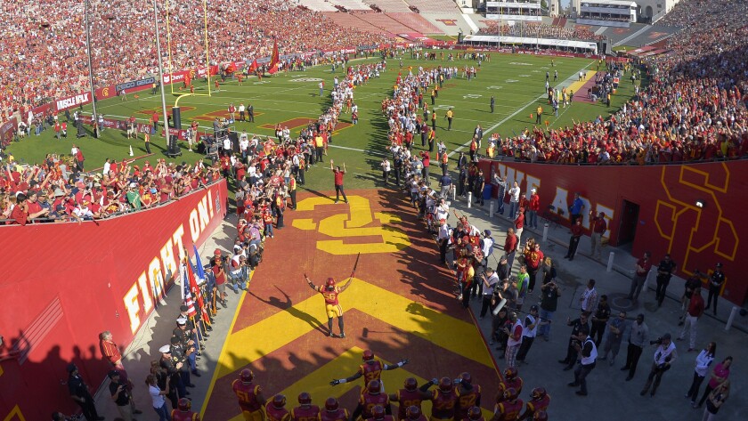 USC football players run onto the field at the Coliseum before a game.