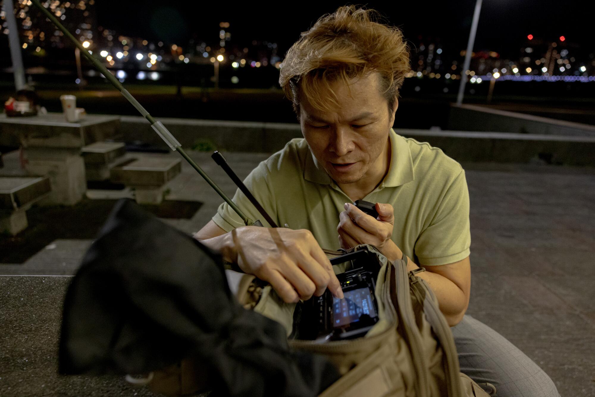 A man looks down while holding a radio unit in a bag 