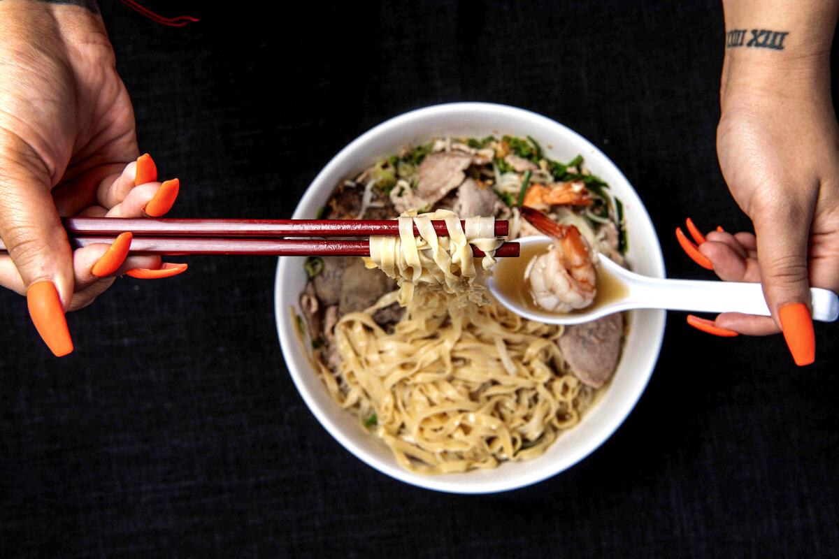 Hands using chopsticks and a white spoon lift noodles out of a bowl of House Special Noodles, served "wet."