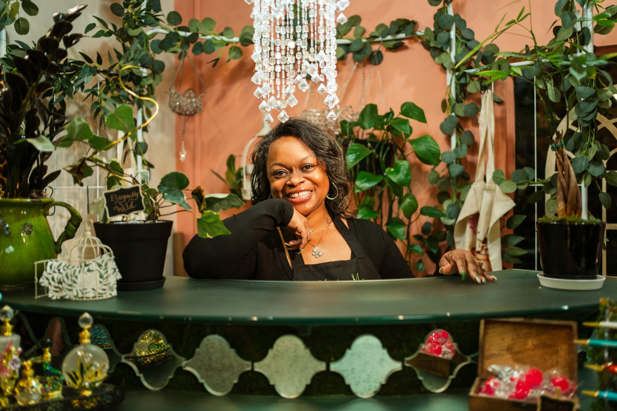 A smiling woman stands behind the green counter in a plant store with peach walls