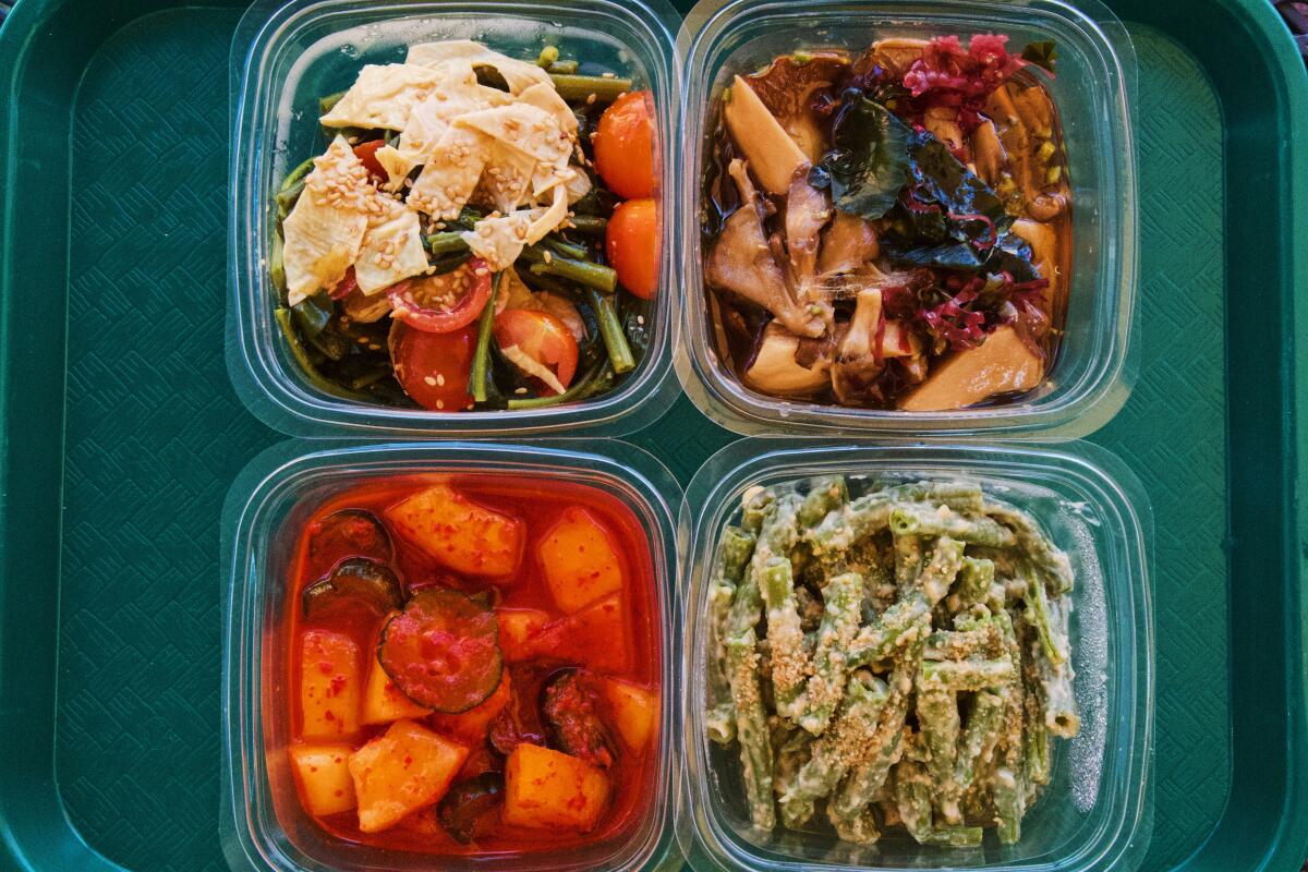 Four banchan on a green tray, from clockwise: yuba, mushrooms, green beans, and fermented melon