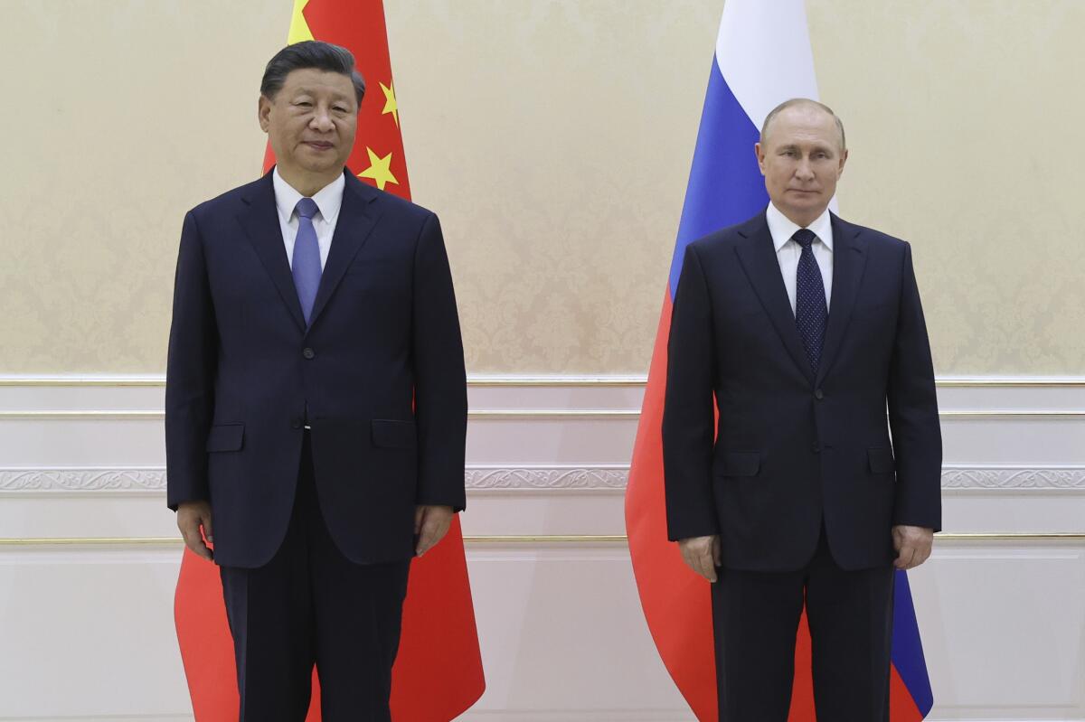 Chinese President Xi Jinping and Russian President Vladimir Putin stand side by side in front of flags.