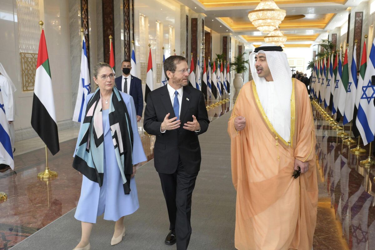The Israeli president and first lady walk with the UAE's foreign minister along a hall lined with Israeli and UAE flags