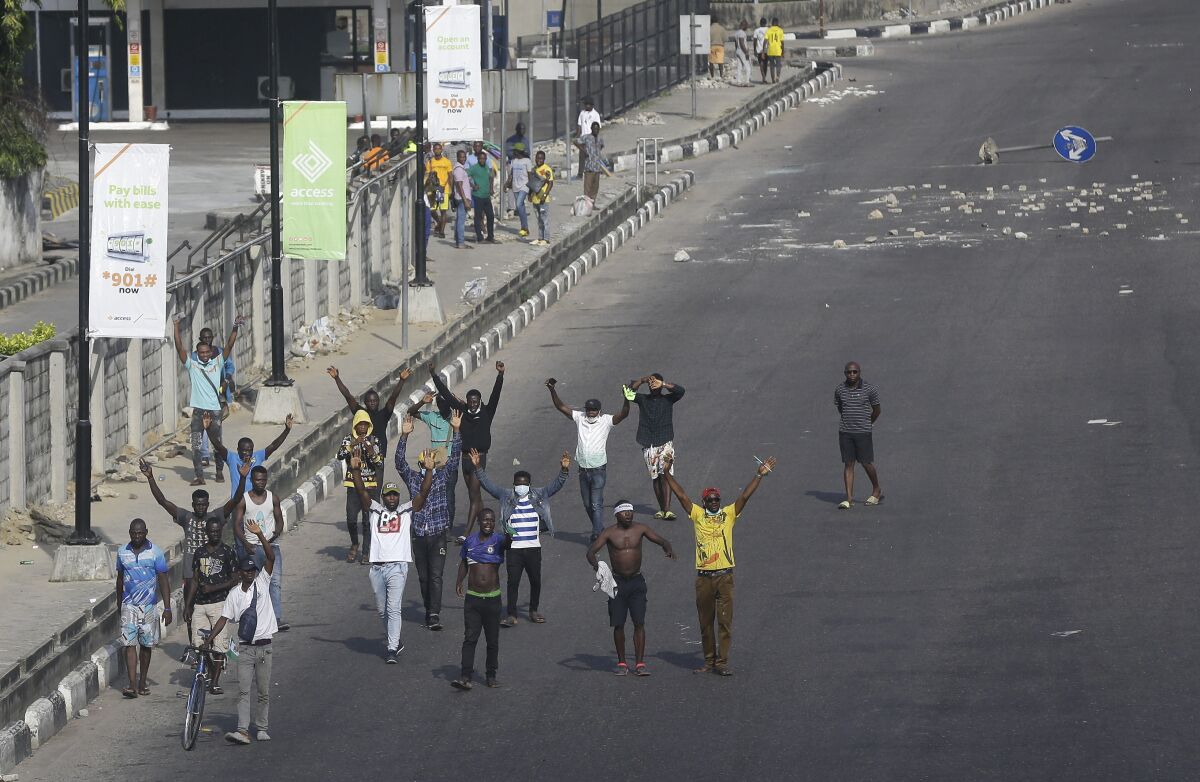 A group of protesters walk down a Nigerian street with arms raised.