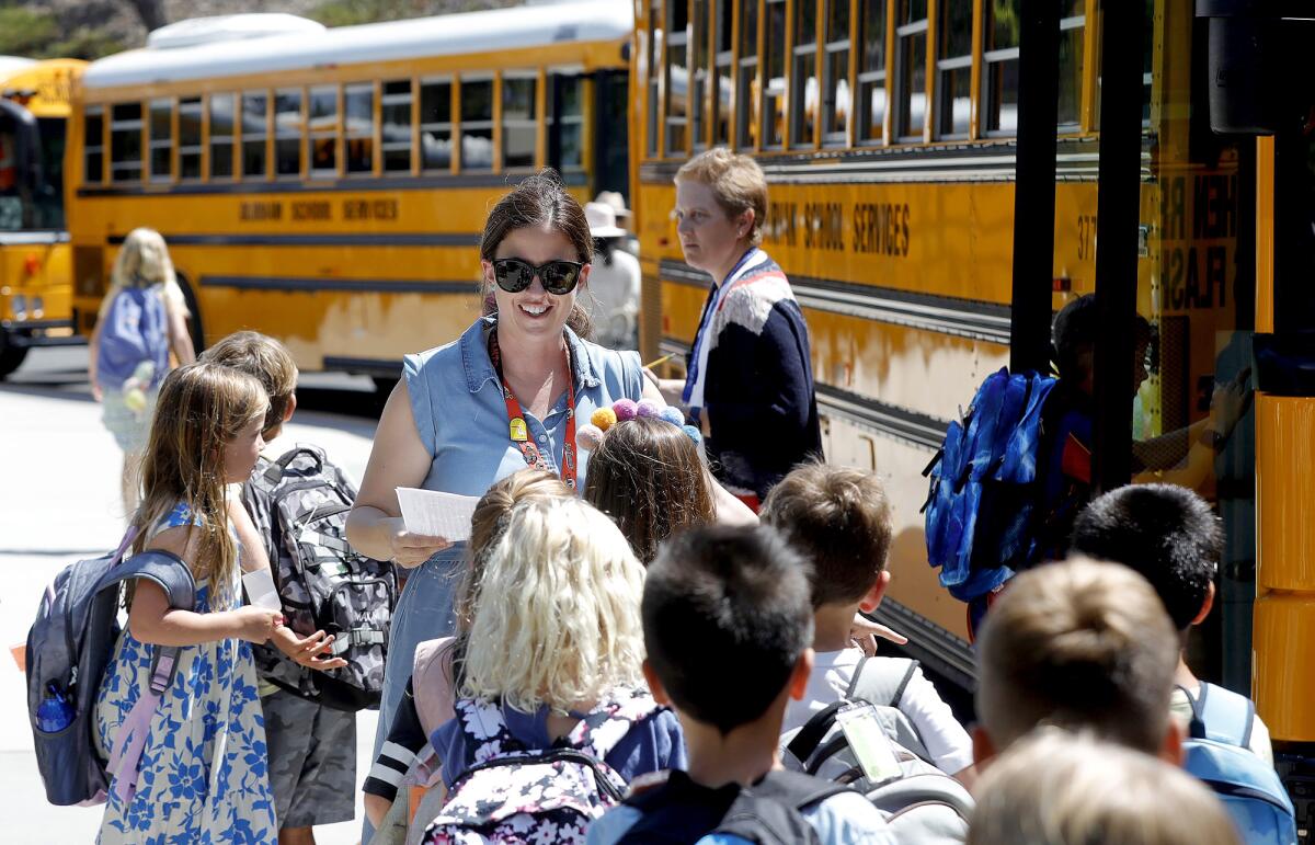 Second-grade teacher Tasa Day leads kids to their home bus during the first day of class at Top of the World Elementary.