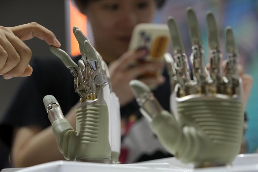 A visitor touches a humanoid robot hand on display at an AI exhibition booth during the The World Artificial Intelligence Conference & High-Level Meeting on Global AI Governance, in Shanghai China, July 4, 2024. (AP Photo/Andy Wong)