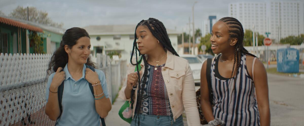 Three young women talk as they walk along a roadway.