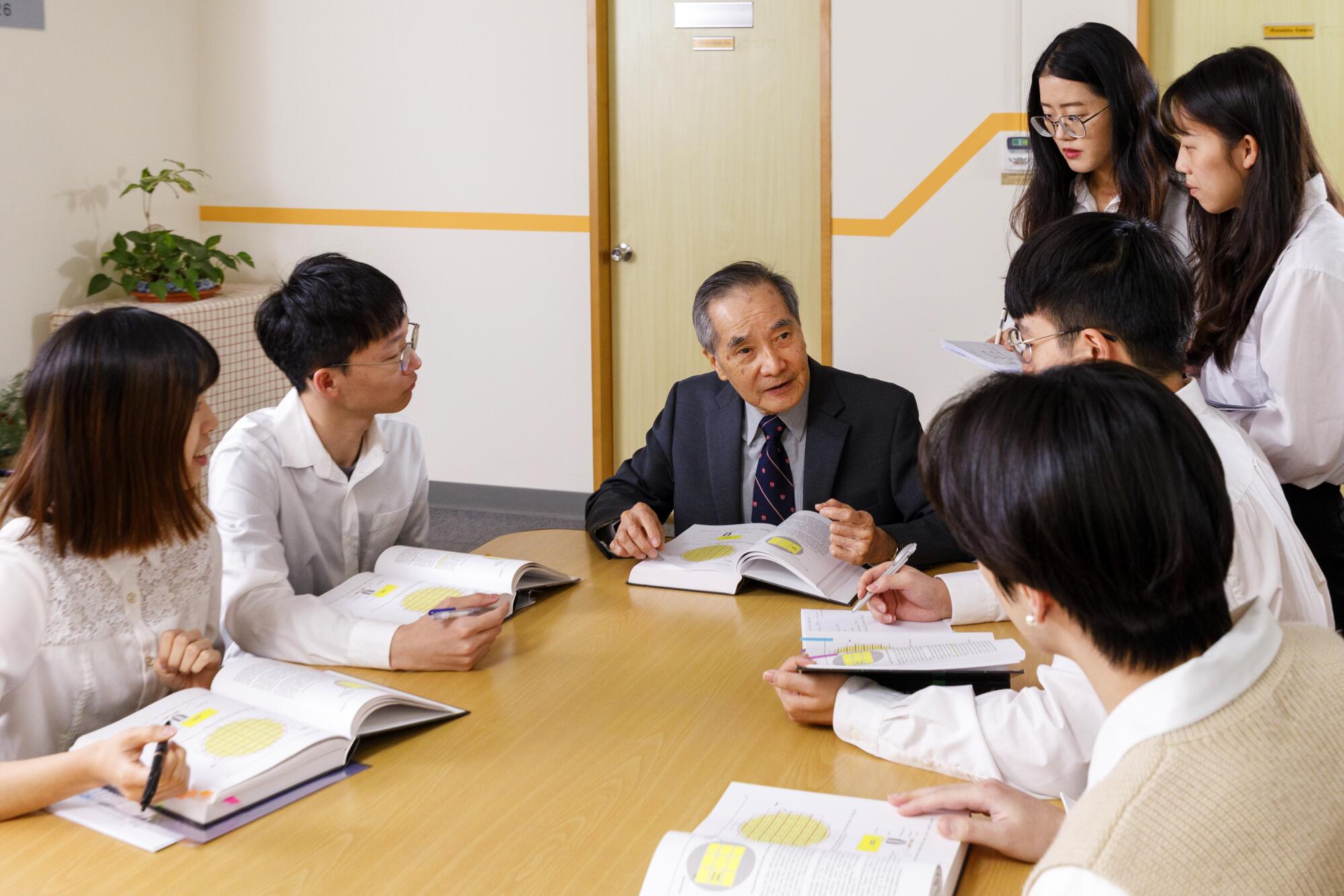 Burn Lin and his students sitting or standing at a table with books open.