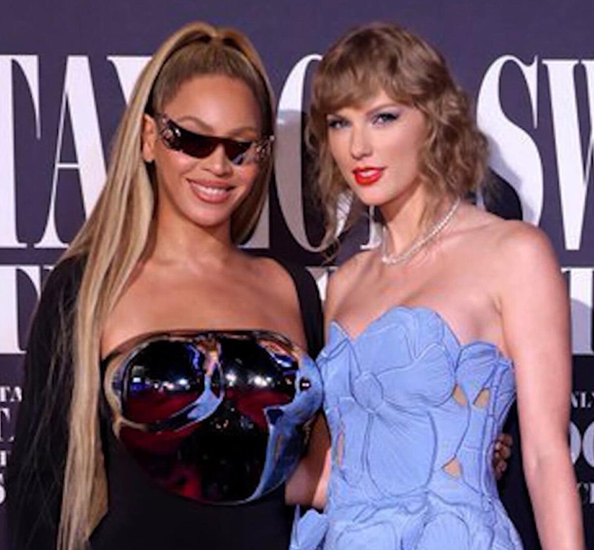 Beyonce in dark glasses and a strapless top and Taylor Swift in a blue dress standing shoulder to shoulder