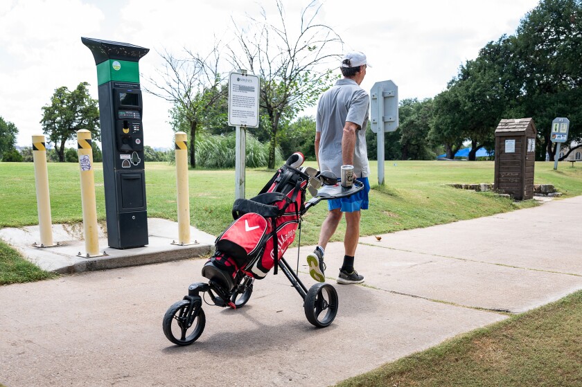 Golf player Mike Riggs pulls his clubs on a wheeled trolley at the Hancock Golf Course in Austin, Texas. 