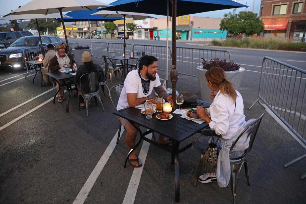 Brandon and Rose Astudillo dine at a restaurant table set up in parking spots alongside a road.