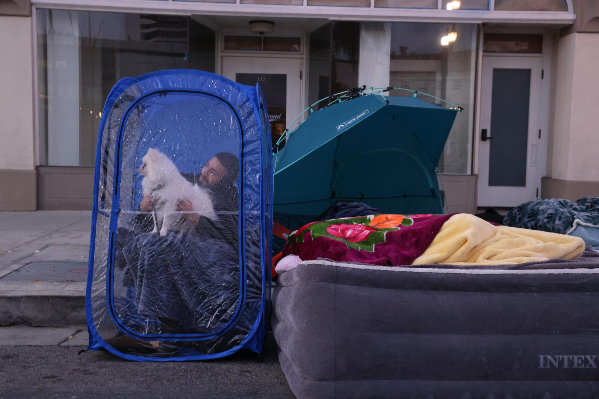 A man with a dog on his lap sits in a plastic container next to an inflatable mattress