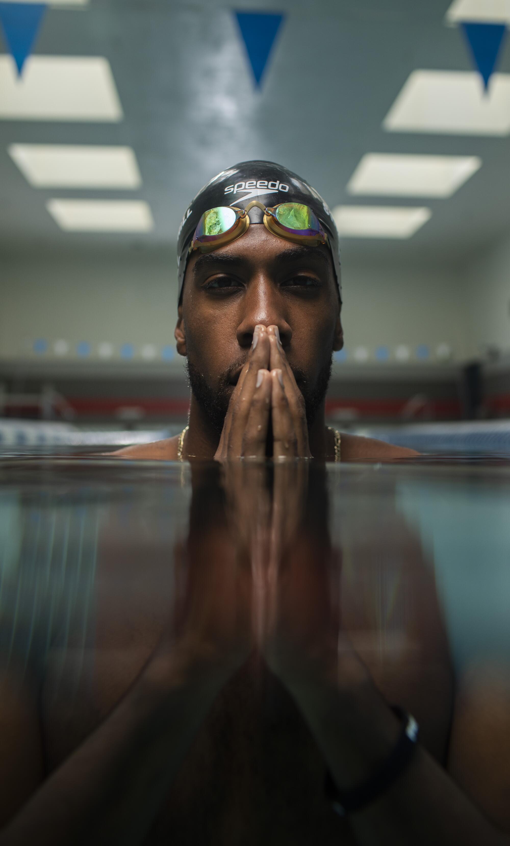 Swimmer Jamal Hill poses neck deep in a pool, with his hands together in front of his mouth and nose