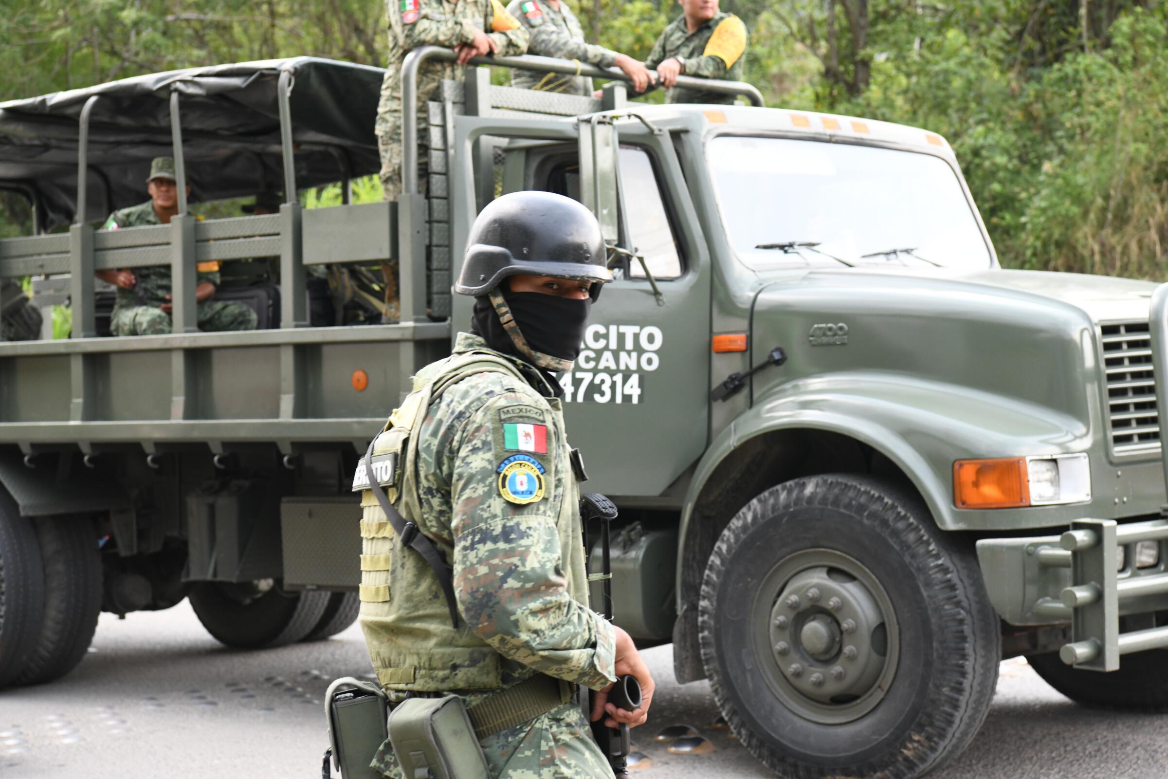 A soldier in helmet and body armor stands near a large green transport truck.