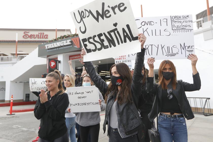 Demonstrators including Valentina Molli, center, and Lindsey Lobianco, right, who both work in the restaurant and cosmetic industries respectfully, protest the recent state closures and stay-at-home orders along Newport Blvd and Triangle Square on Monday.