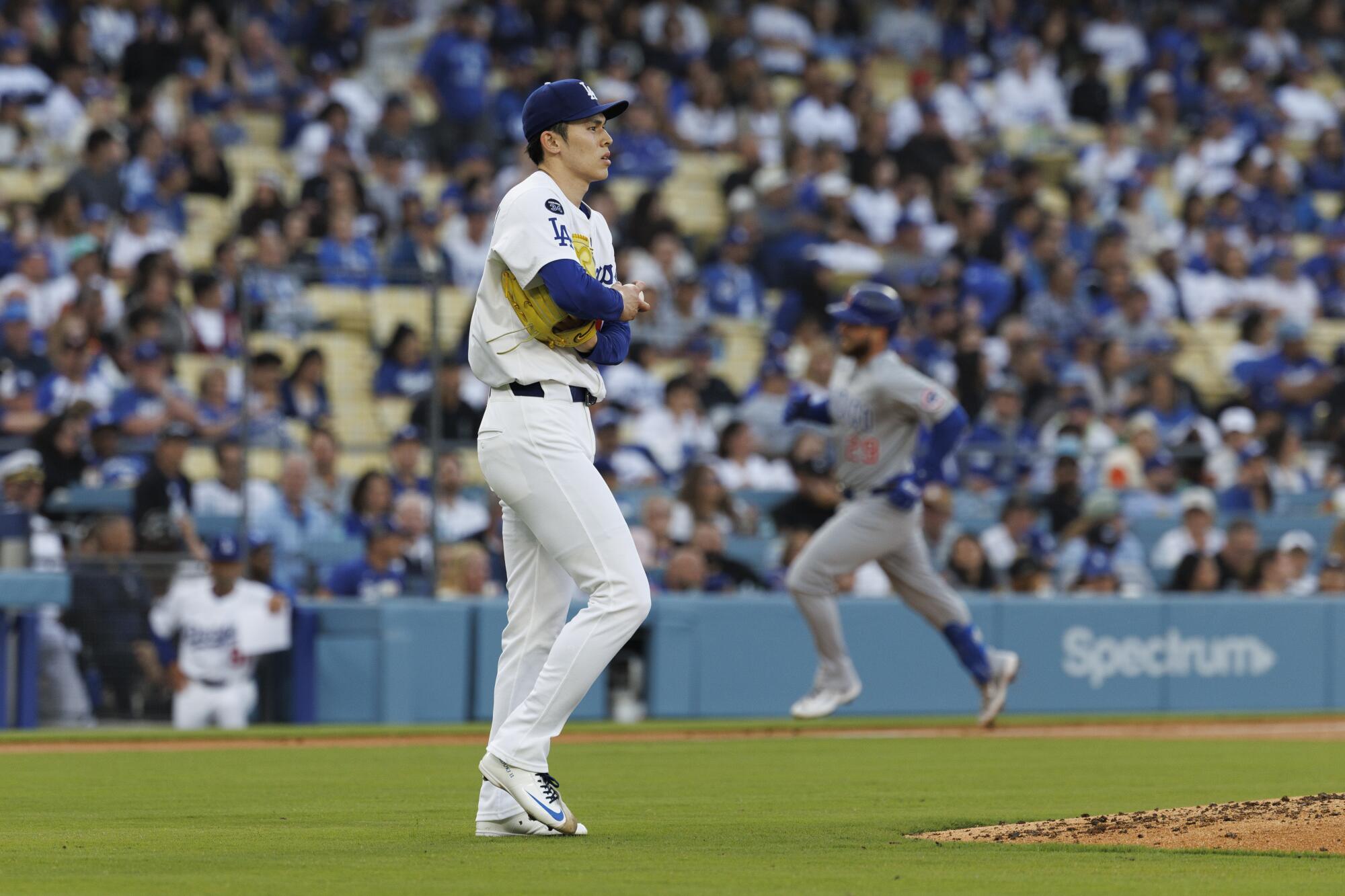 Roki Sasaki walks to the mound as Michael Busch runs the bases.