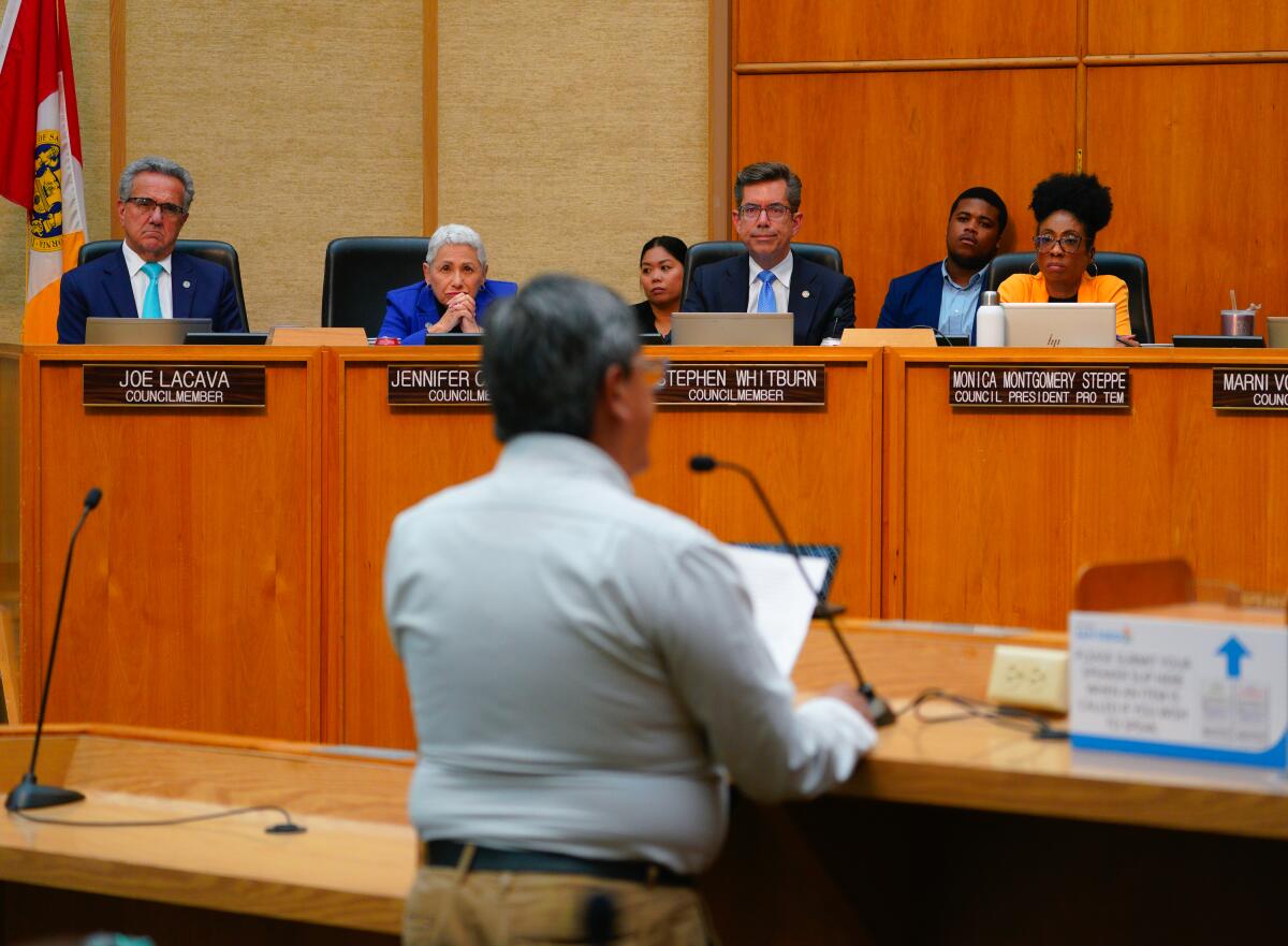 A man speaks at a microphone before City Council members seated at a dais.