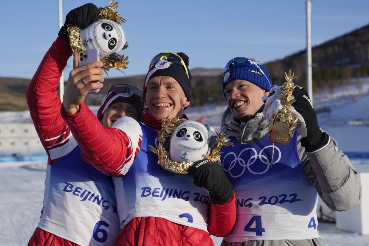 Gold medal finisher Russian athlete Alexander Bolshunov takes a selfie with silver medal finisher Russian athlete Denis Spitsov, left, and bronze medal finisher Finland's Iivo Niskanen after the men's 15km + 15km skiathlon cross-country skiing competition at the 2022 Winter Olympics, Sunday, Feb. 6, 2022, in Zhangjiakou, China. (AP Photo/Aaron Favila)