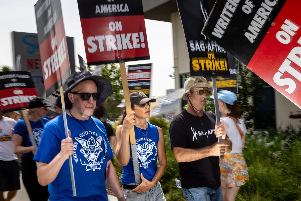 Three figures hold WGA signs on the picket line.