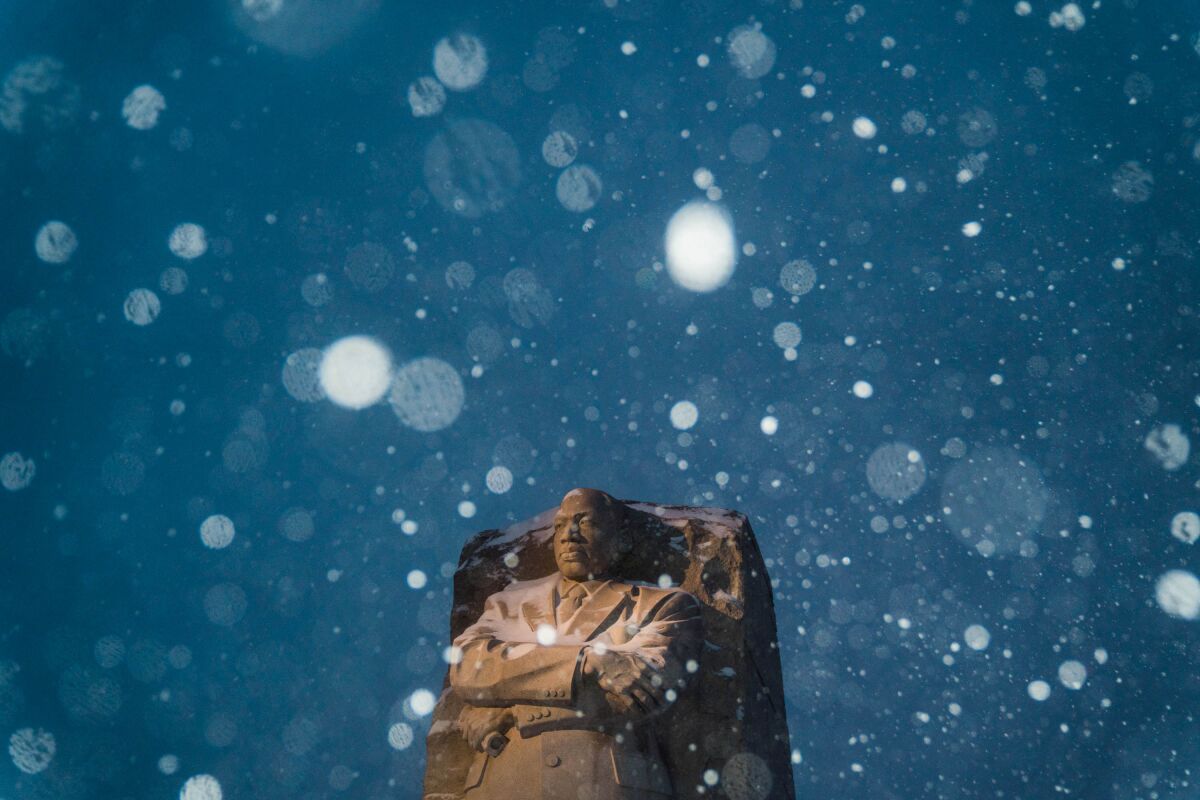 Snow looks like bright round white spots descending over a statue of Martin Luther King Jr.
