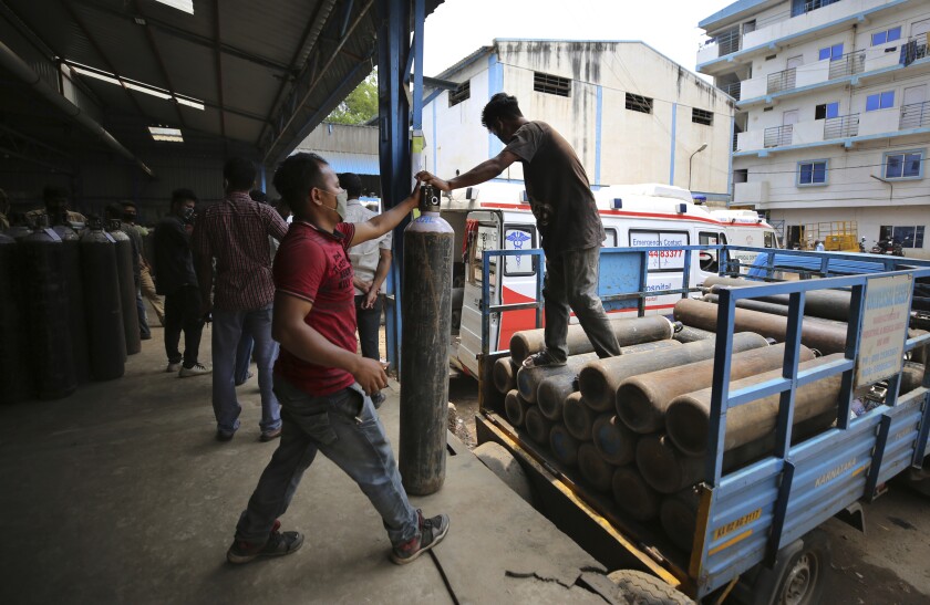 Two workers unload empty oxygen cylinders from a vehicle.