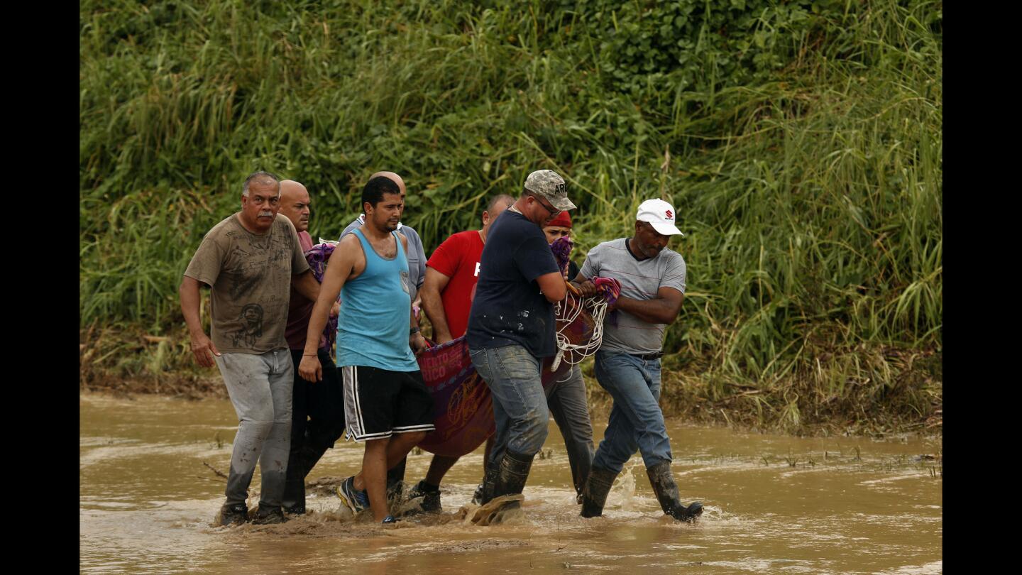 Edwin Vidal, 61, a retired member of the U.S. Army special forces, far left, and other men carry Delia Piñeda, 89, from Salto Arriba as they evacuate her from an area cut off from Utuado.