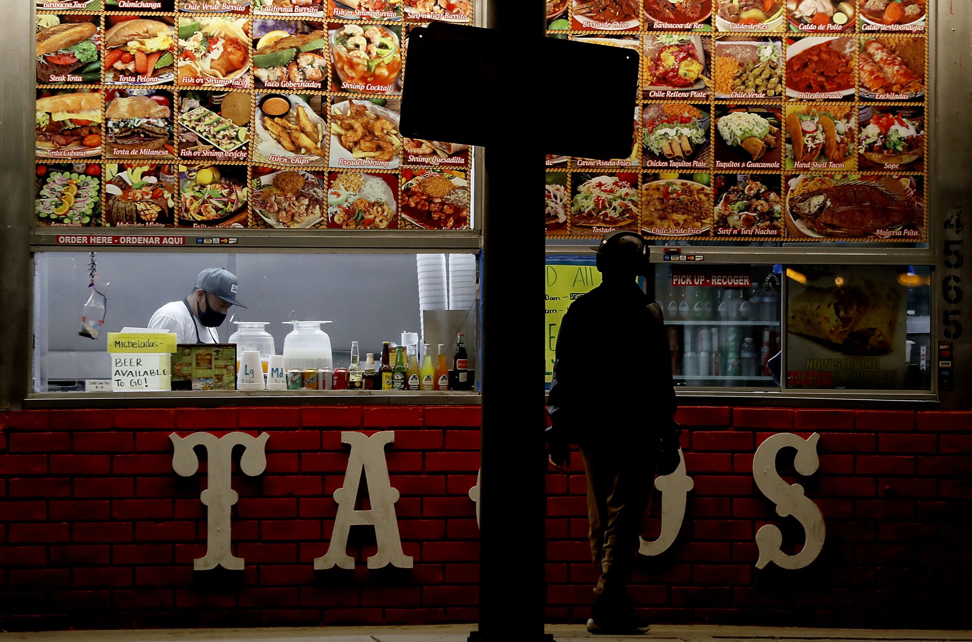A restaurant worker completes a takeout order for a customer at a taco stand along Redondo Beach Boulevard in Hermosa Beach.