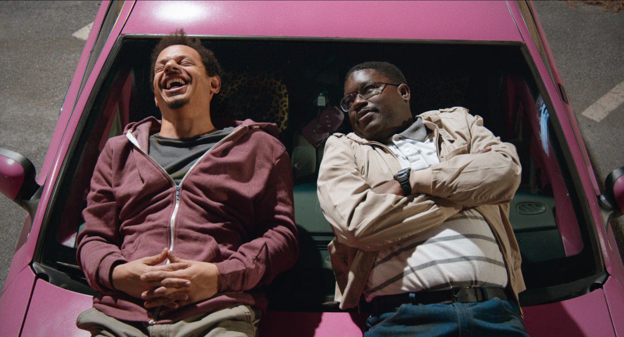 Eric Andre and Lil Rel Howery sit on the hood of a pink car