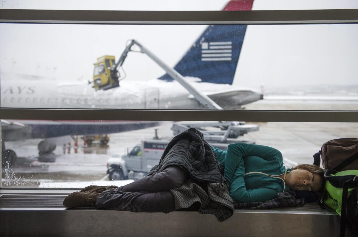 A stranded passenger naps while a work crew deices a plane at Reagan National Airport in Arlington, Va., on March 17. Winter storms drove airline cancellations in March.