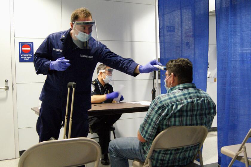 U.S. Coast Guard health technician Nathan Wallenmeyer, left, and customs supervisor Sam Ko screen a passenger who arrived from Sierra Leone at O'Hare International Airport in Chicago.