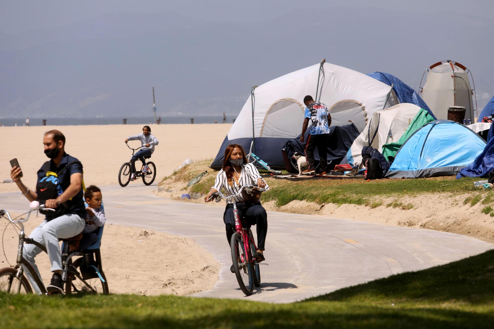 Bicyclists ride past tents on Venice Beach.