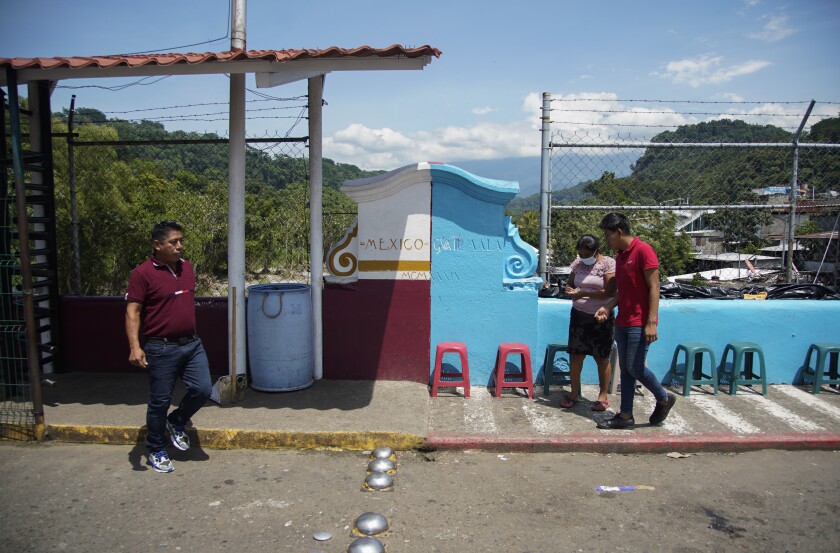 A man walks south toward Guatemala and a man and woman walk north to Mexico near a painted line marking the border