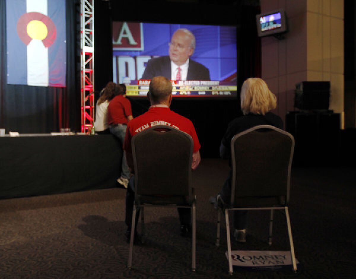 A couple sits on chairs in a near-empty room to watch Fox News commentator Karl Rove on a big-screen television during a Republican Party election night gathering in the club level of Sports Authority Field at Mile High in Denver on Tuesday.
