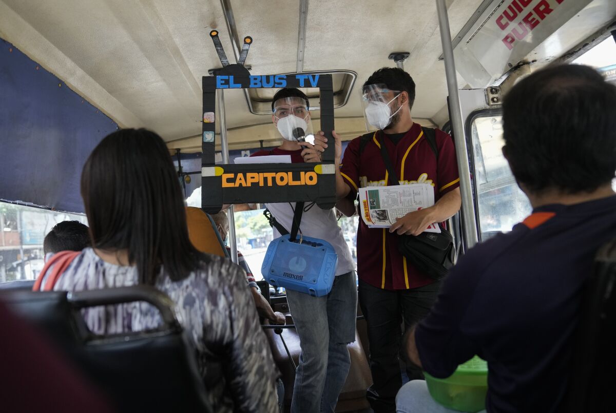 Juan Pablo Lares, right, holds a cardboard frame in front of his associate Maximiliano Bruzual who reads their newscast "El Bus TV Capitolio" to commuters on a bus in Caracas, Venezuela, Saturday, July 31, 2021. Two decades of governments that see the press as an enemy have pushed Venezuelan journalists to find alternative ways to keep citizens informed. (AP Photo/Ariana Cubillos)