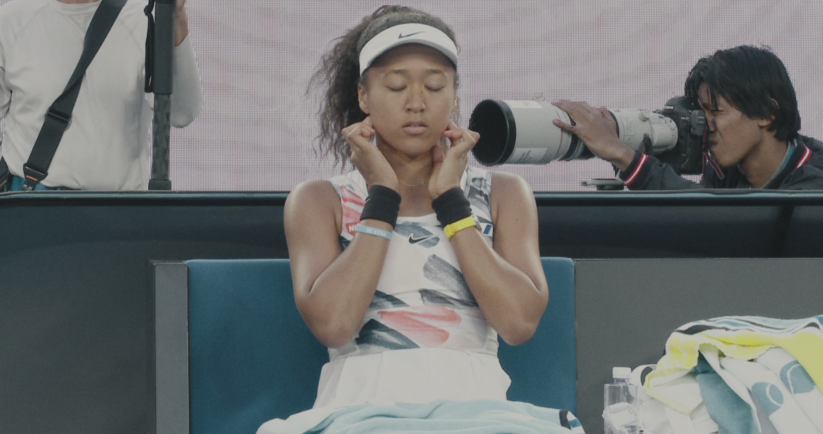 Naomi Osaka sitting courtside with her eyes closed.