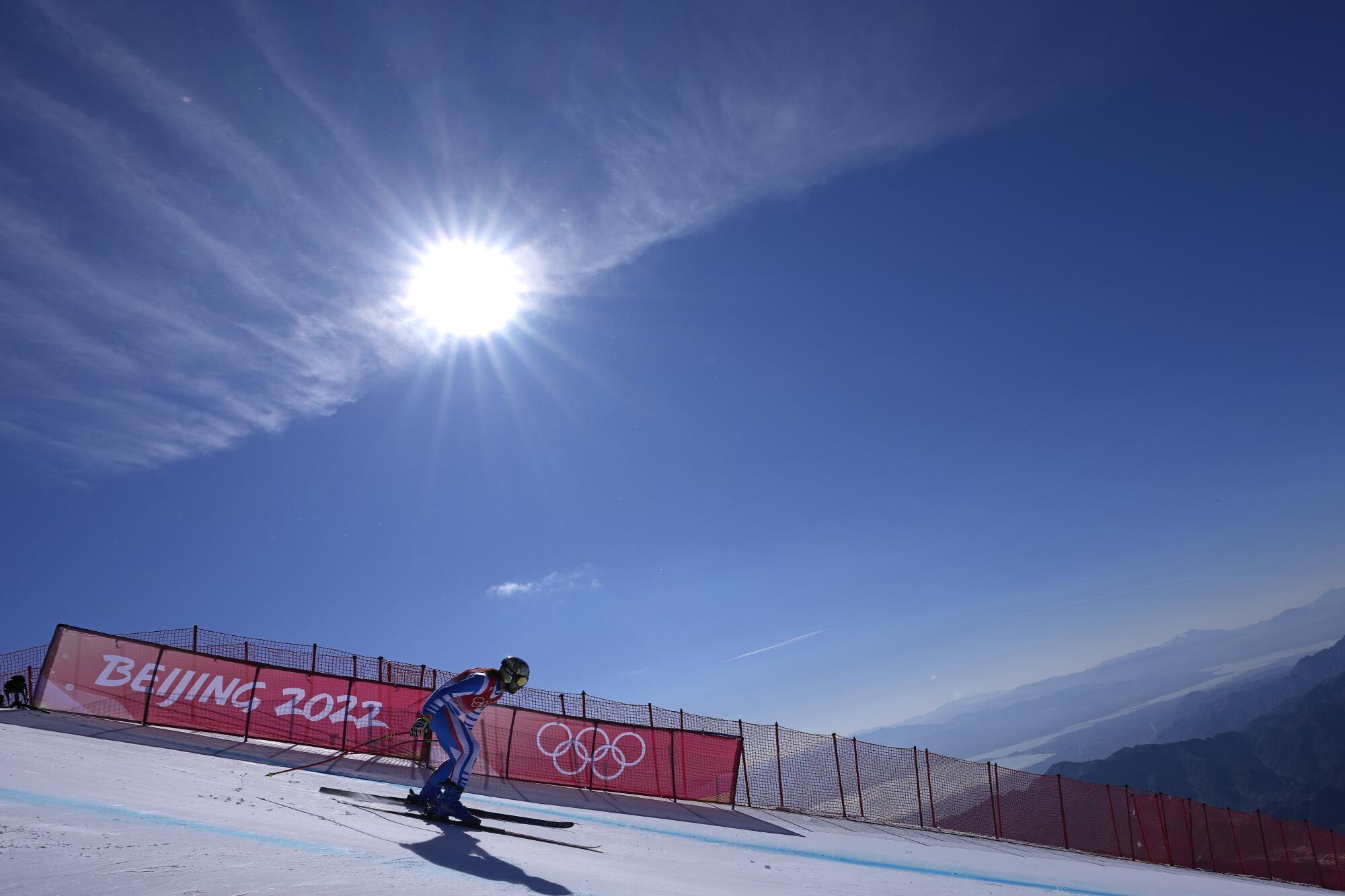 A skier on the slopes, with a red banner with the words Beijing 2022 and five rings in the background 