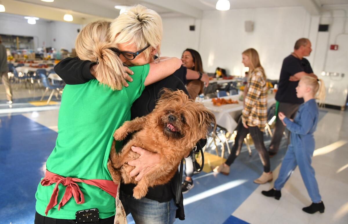 Robin Levy, whose home burned down in Malibu, holds her dog Violet while being hugged by friend Yvette Kleiser at a "Happy Friendsgiving" at Santa Monica High School on Tuesday.