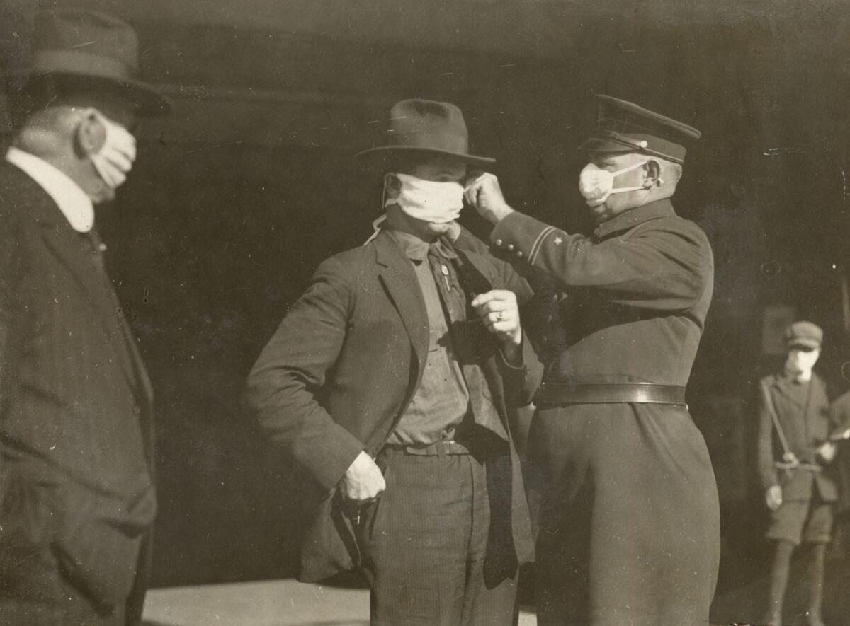 A police officer adjusts a man’s flu mask in San Francisco during the 1918 pandemic.