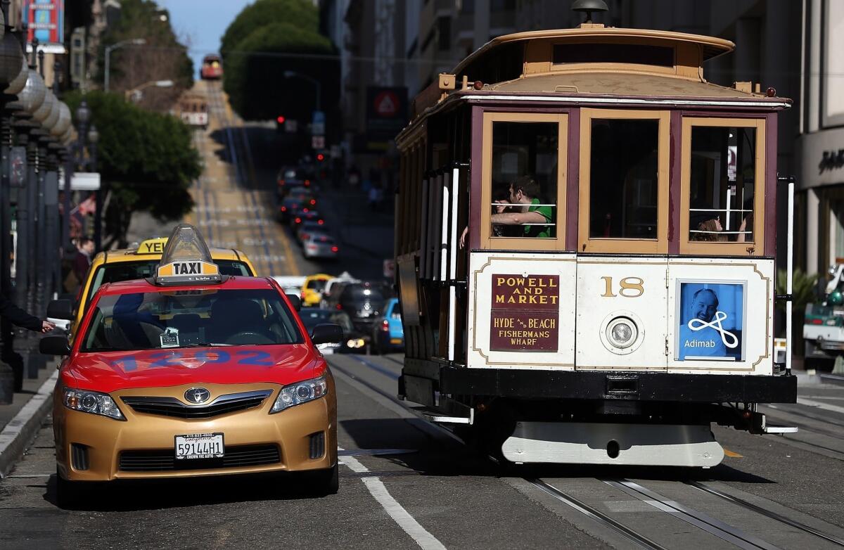 A cable car passes a line of taxicabs in San Francisco. The San Francisco Cab Driver Assn. says that nearly one-third of the city's licensed taxi drivers have started to drive for ride-sharing services such as Lyft, Uber and Sidecar.