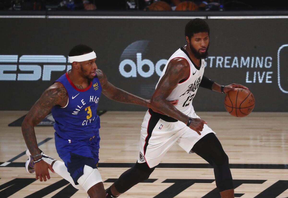 Clippers' guard Paul George controls the ball while defended by Denver Nuggets forward Torrey Craig.