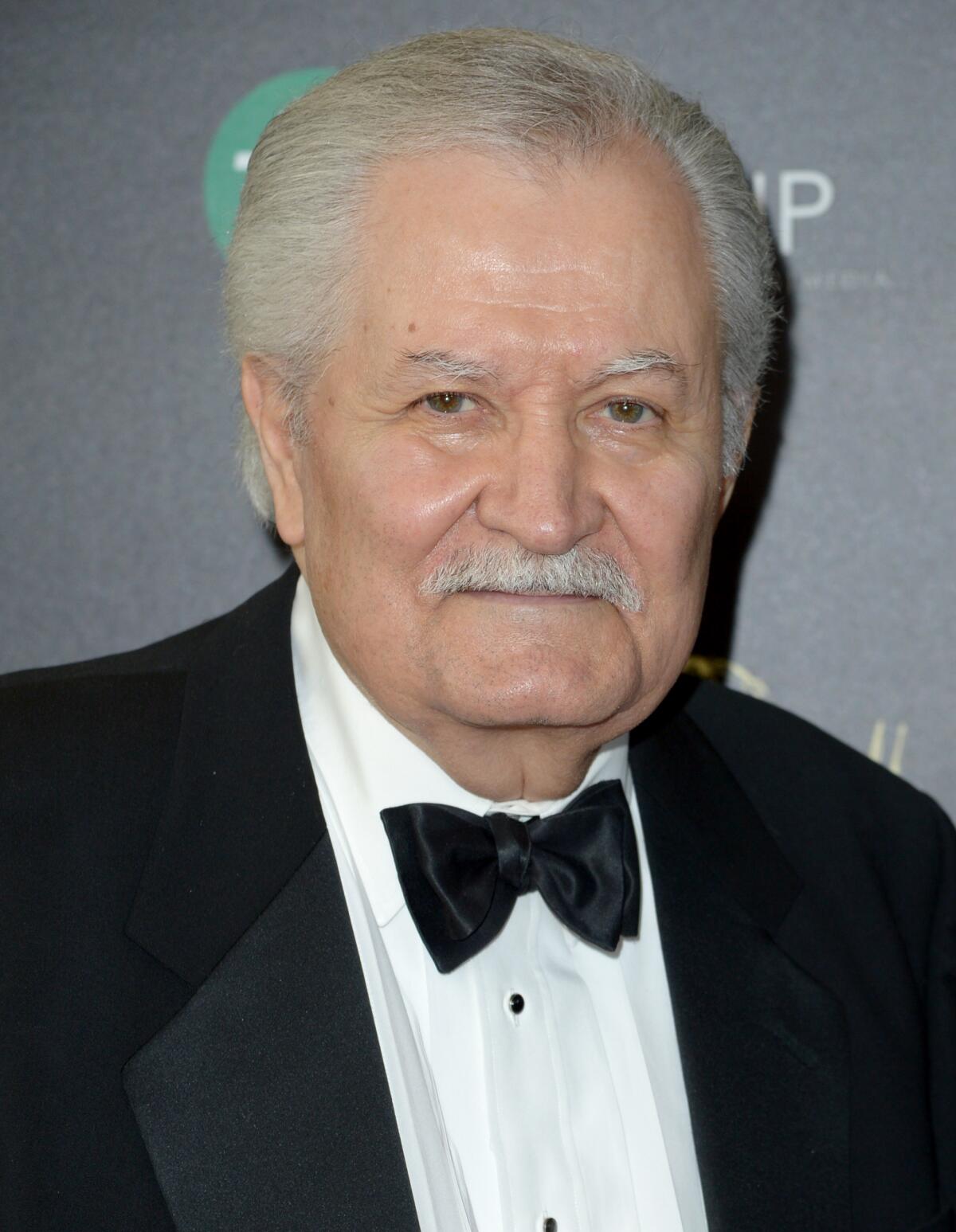 An older man with white hair and a mustache wears a tuxedo