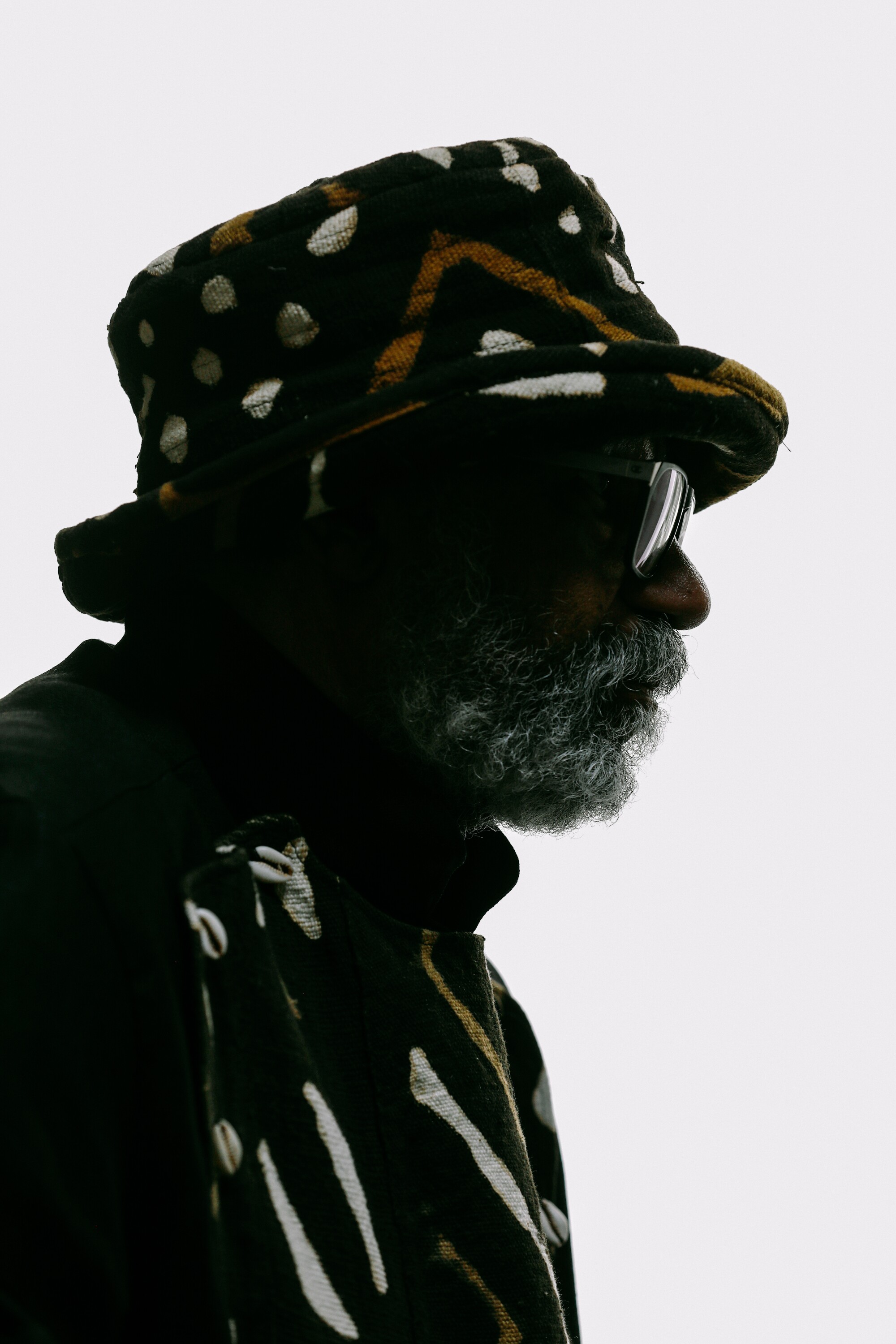 Artist Ulysses Jenkins is seen in profile wearing a patterned hat in dramatic contrast with a white background