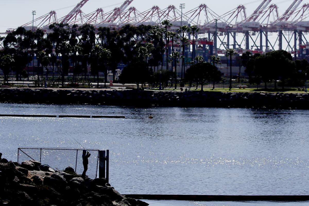 A fisherman casts a line into the mouth of the Los Angeles River near a port complex