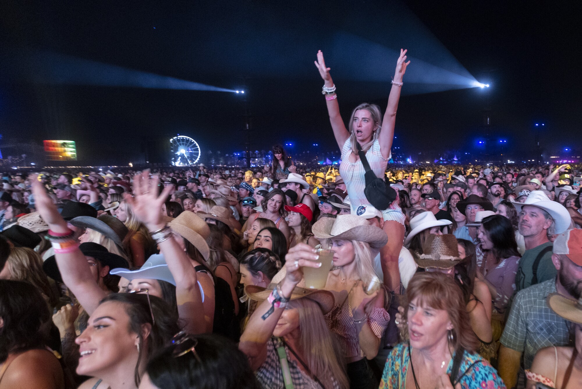A woman sits on the shoulders of a friend as a crowd cheers and sings while watching Maren Morris perform