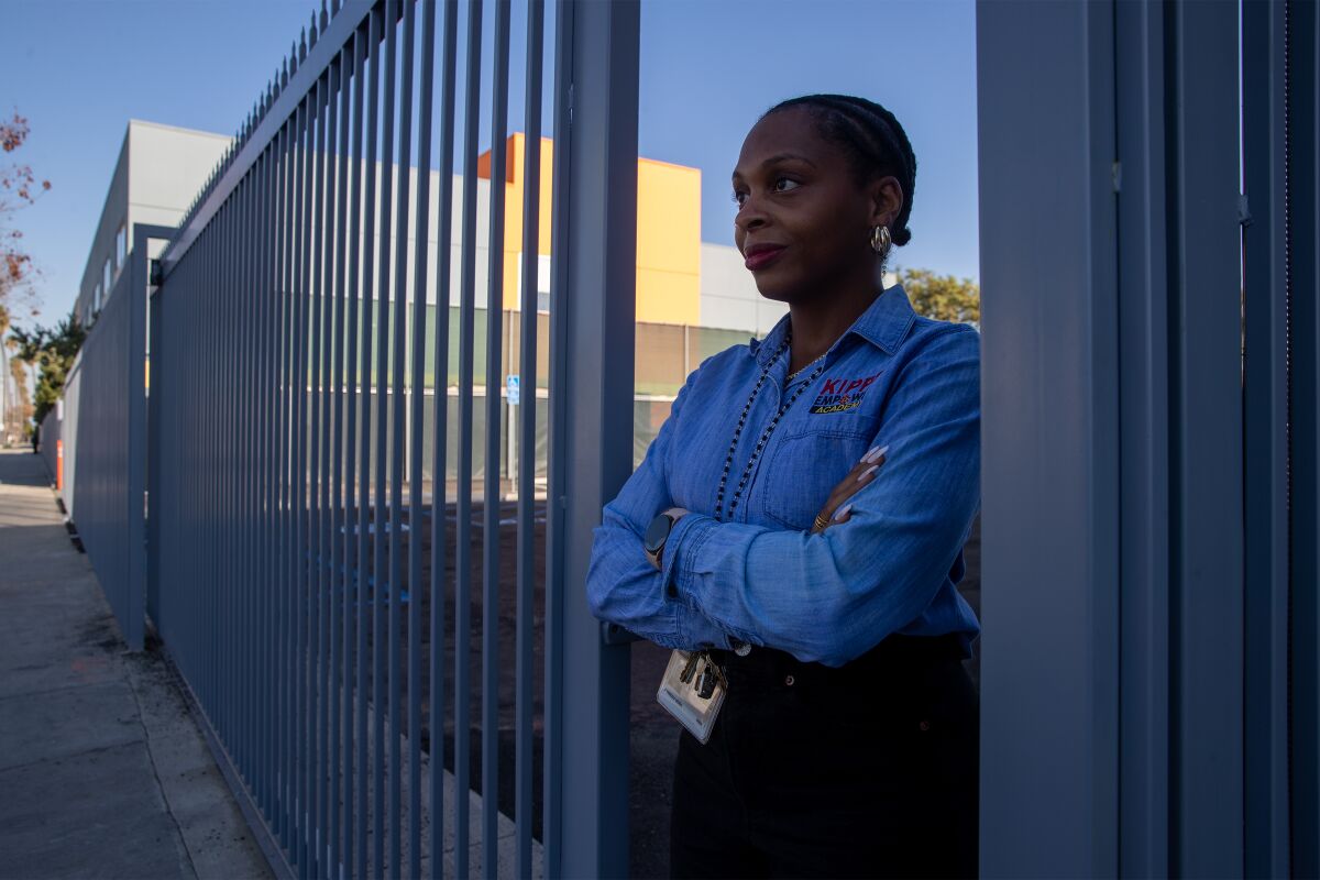 KIPP Principal Chinedu Udeh stands at a gate facing a parking lot. 
