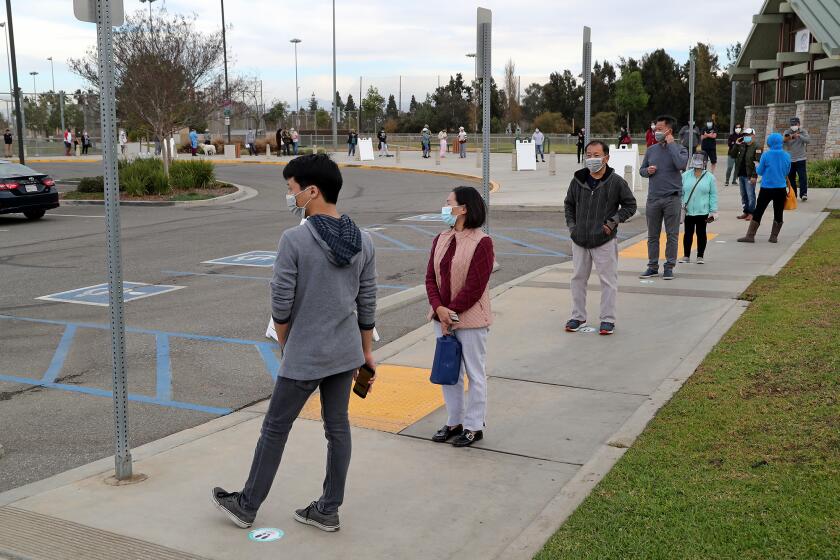 A line of patients wraps around a parking lot sidewalk during a Clinic 360 COVID-19 mobile testing site at Fountain Valley Sports Park on Tuesday morning.