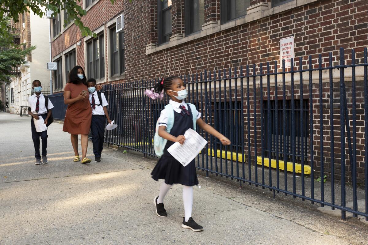 A girl leads her mother and brothers as they arrive at Brooklyn's PS 245, Monday, Sept. 13, 2021, in New York. Classroom doors are swinging open for about a million New York City public school students in the nation's largest experiment of in-person learning during the coronavirus pandemic. (AP Photo/Mark Lennihan)