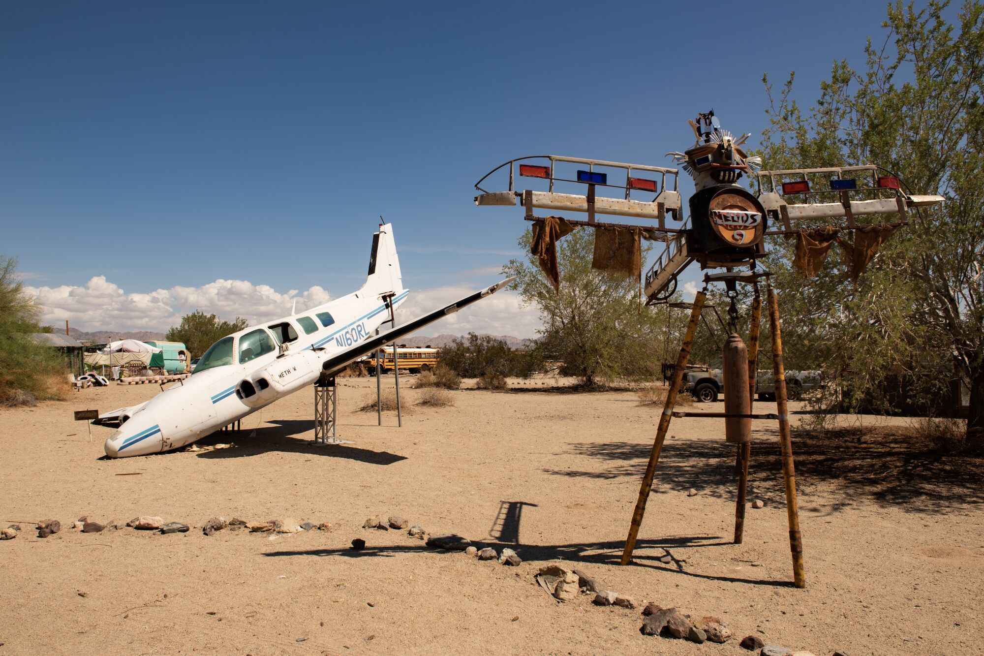 A white single-engine airplane lies nose down, left, and a sculpture made from scrap metal.