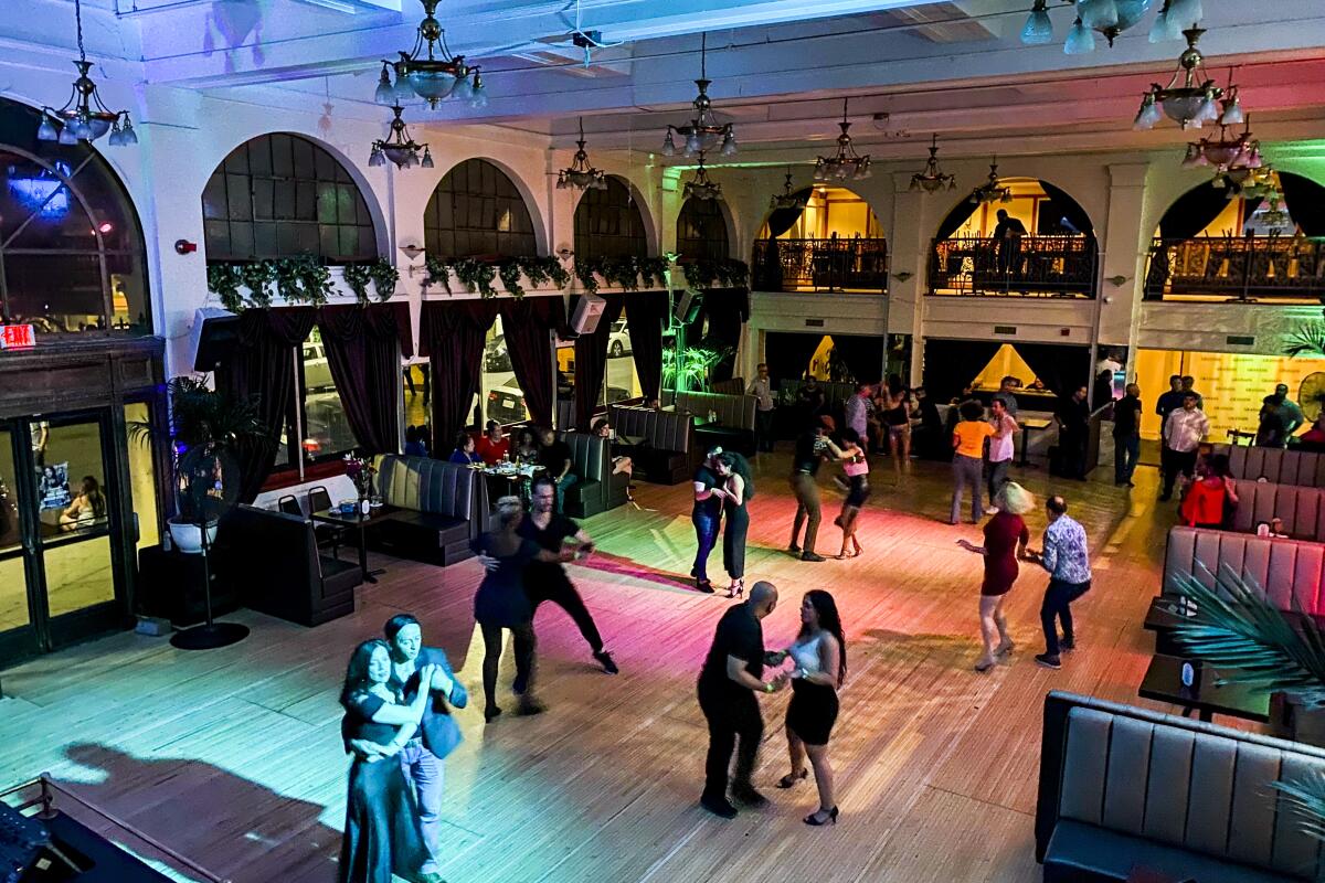 Partners dance on an uncrowded dance floor under colored lights.